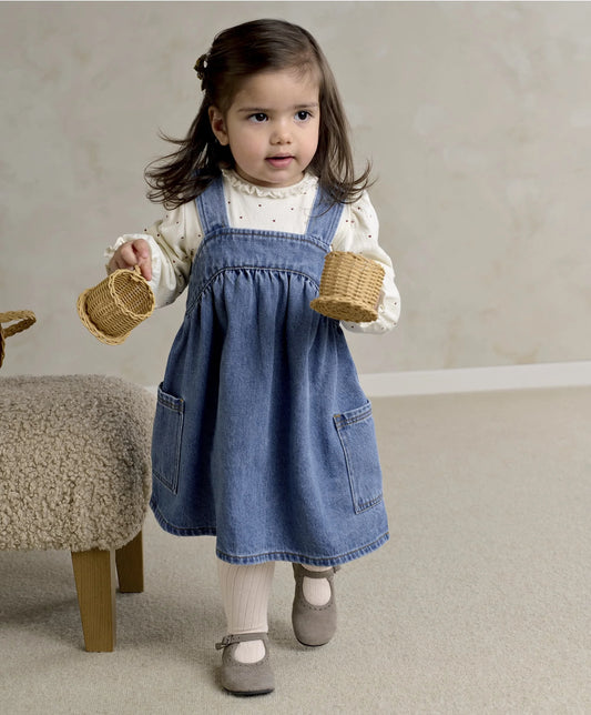 Blue denim pinafore dress with chest buttons over white heart-print long-sleeve bodysuit