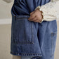 Blue denim pinafore dress with front patch pockets and topstitching over white bodysuit