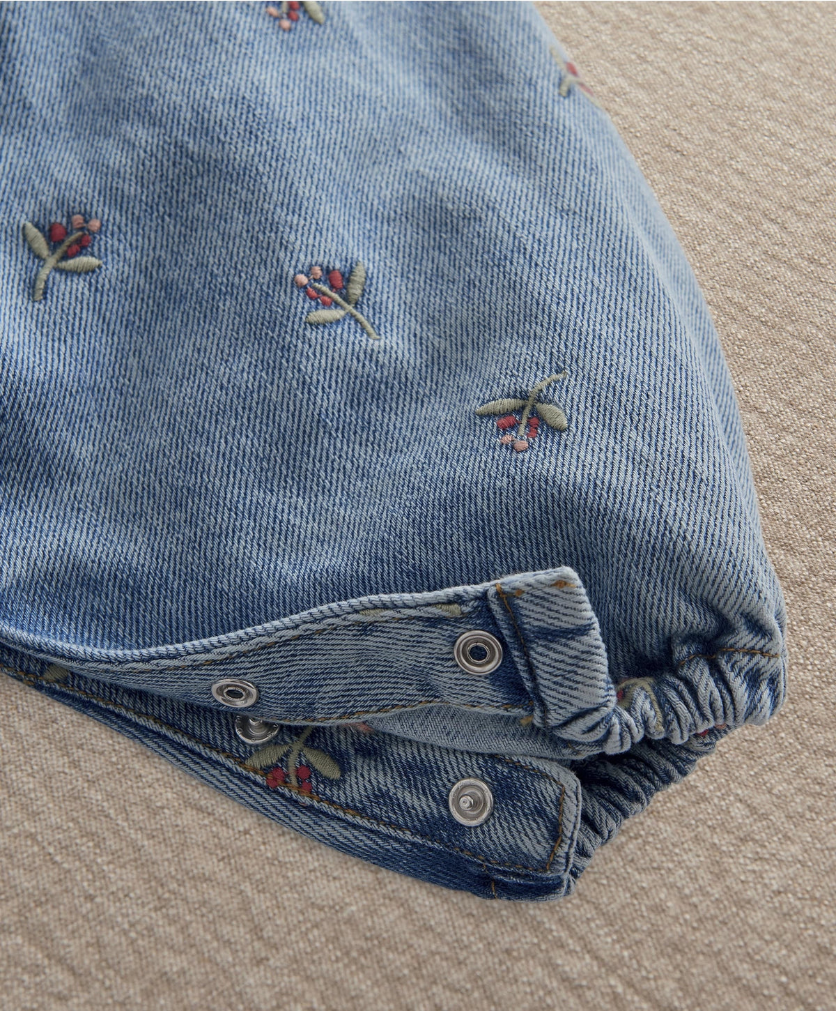 Light blue denim dungaree leg with snap buttons at cuffs and embroidered bow detail