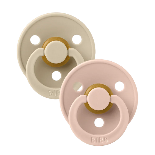 Two round latex baby pacifiers, blush pink and vanilla beige with gold accents