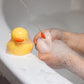 Silicone bath duck toys floating in water, held under running stream