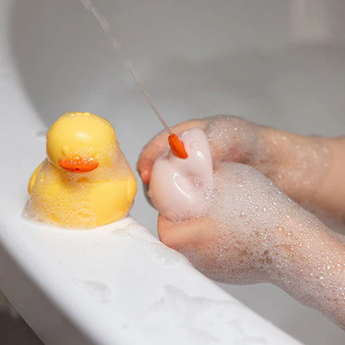 Silicone bath duck toys floating in water, held under running stream