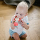 Baby holding red rattle teether with pink flower head and mint teether handle