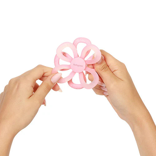 Pink silicone flower teether held by two hands, petal loops and finger grip