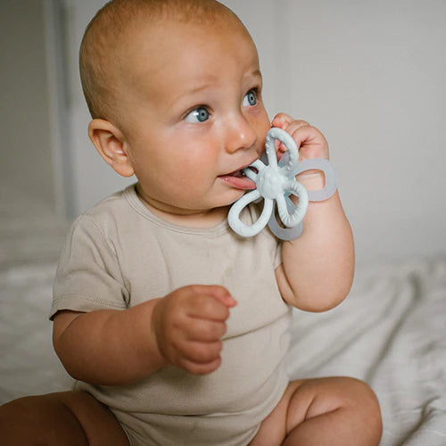 Light blue silicone flower teether held by a baby with ring handles