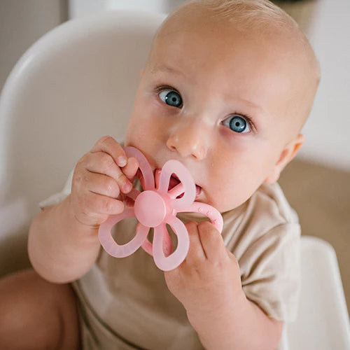 Pink silicone flower teether with ring handles in baby's hands