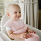 Pink silicone bib on baby, adjustable neck band and curved front pocket visible
