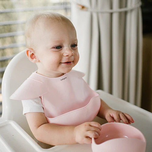 Pink silicone bib on baby, adjustable neck band and curved front pocket visible
