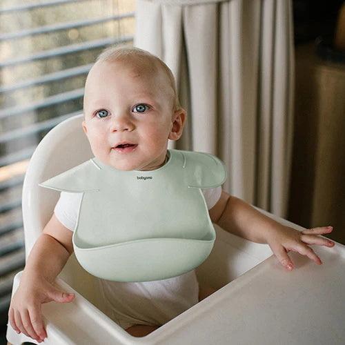 Mint silicone baby bib with adjustable lock, toddler wearing bib at feeding tray