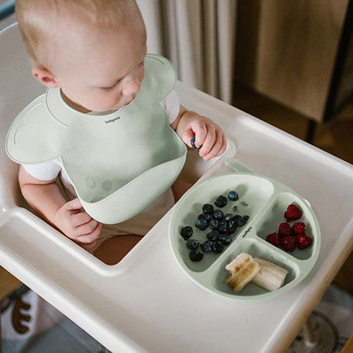 Mint silicone baby bib with adjustable lock, worn by toddler at high chair