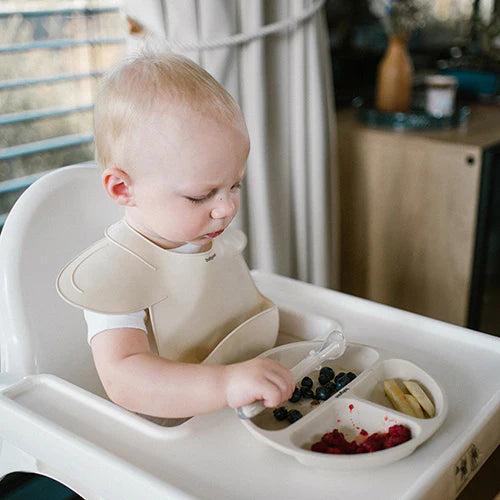 Beige silicone bib on baby with adjustable neck strap and deep catch pocket