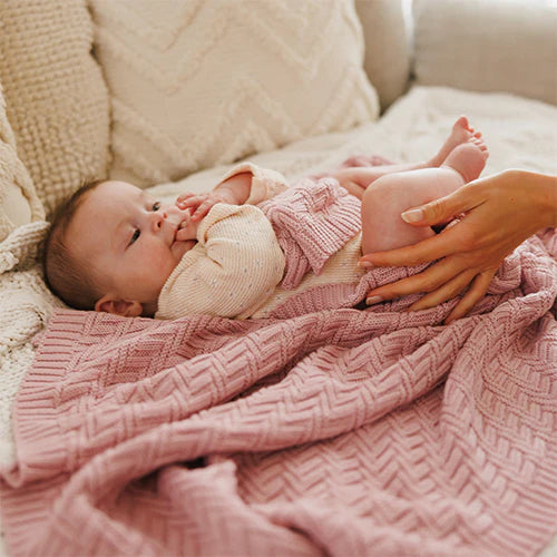 Pink knitted cotton blanket with baby wrapped in the herringbone-style knit