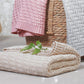 Pink knitted cotton blanket with folded chevron pattern edge, layered with neutral throw