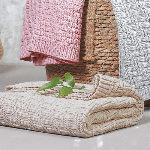 Pink knitted cotton blanket with folded chevron pattern edge, layered with neutral throw