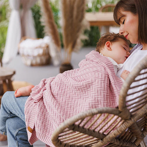 Pink knitted cotton blanket draped over a baby, with chunky chevron texture