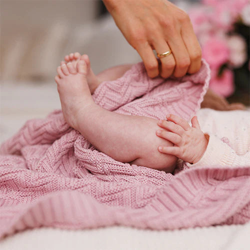 Pink knitted cotton blanket close-up, baby feet tucked under textured knit