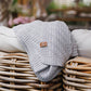 Grey cotton knitted blanket with chevron knit, folded over a seating surface