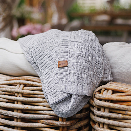 Grey cotton knitted blanket with chevron knit, folded over a seating surface