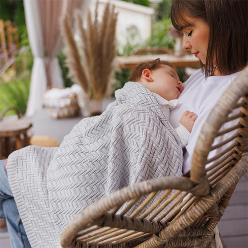 Grey cotton knitted blanket with chevron texture draped over a child being held