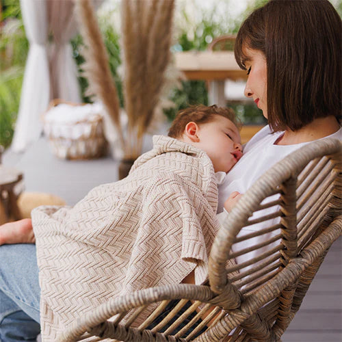 Cotton knitted blanket in beige with chevron knit texture, wrapped around baby