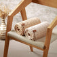 Merino wool blanket, dark beige, rolled and stacked on a sofa chair