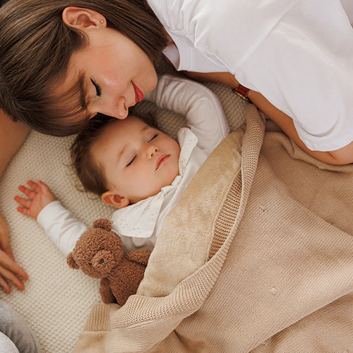 Beige flannel-lined cotton blanket wrapped around a child, knit border visible