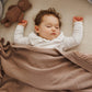 Cotton blanket with flannel lining draped over baby, tan fabric with visible knit border