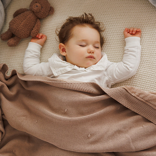 Cotton blanket with flannel lining draped over baby, tan fabric with visible knit border