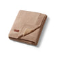 Cotton blanket with flannel lining, folded tan with stitched edge and small label