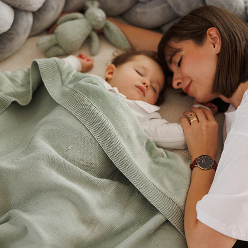 Green blanket with flannel lining draped over a baby for cozy coverage