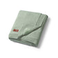 Green cotton blanket with flannel lining, folded with stitched edge and small logo tag