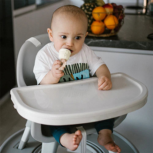 Beige baby food feeder held by an infant with mesh nipple and twist ring