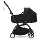 Black stroller with attached newborn carrycot and hood, front wheels and handle visible.