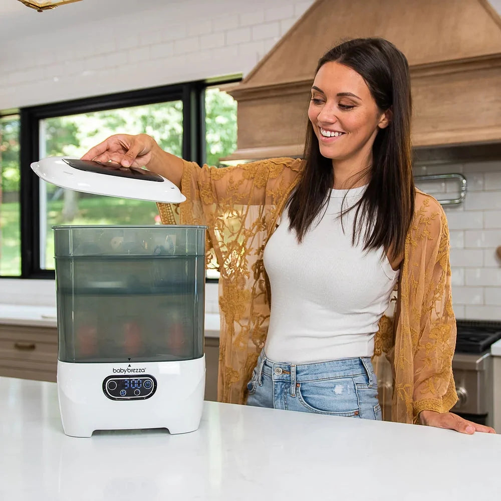 Baby bottle sterilizer dryer beside kitchen counter, lid being lifted by a person.