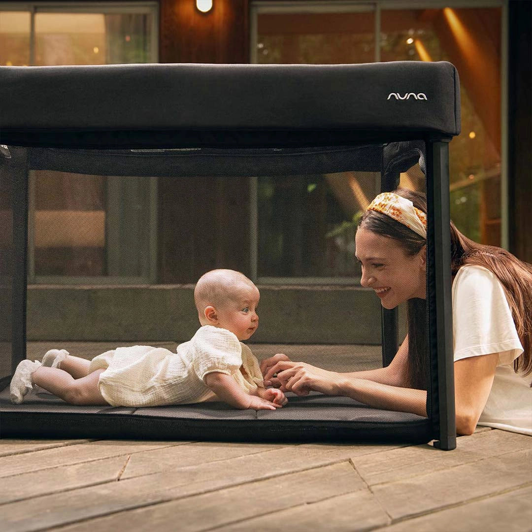 Black playard with mesh sides and canopy, with baby inside