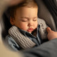 Beige car seat holding a sleeping baby, padded headrest and shoulder straps