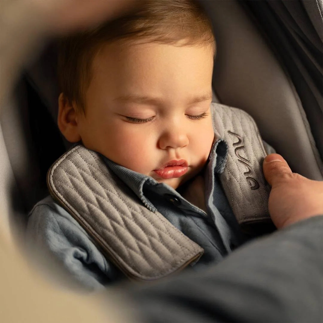 Beige car seat holding a sleeping baby, padded headrest and shoulder straps