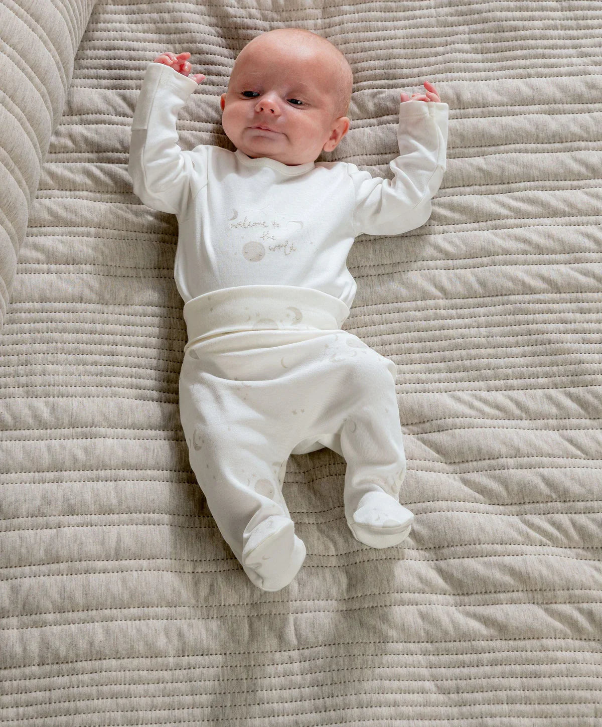 White footed baby bodysuit set with long sleeves and space print, lying on quilt