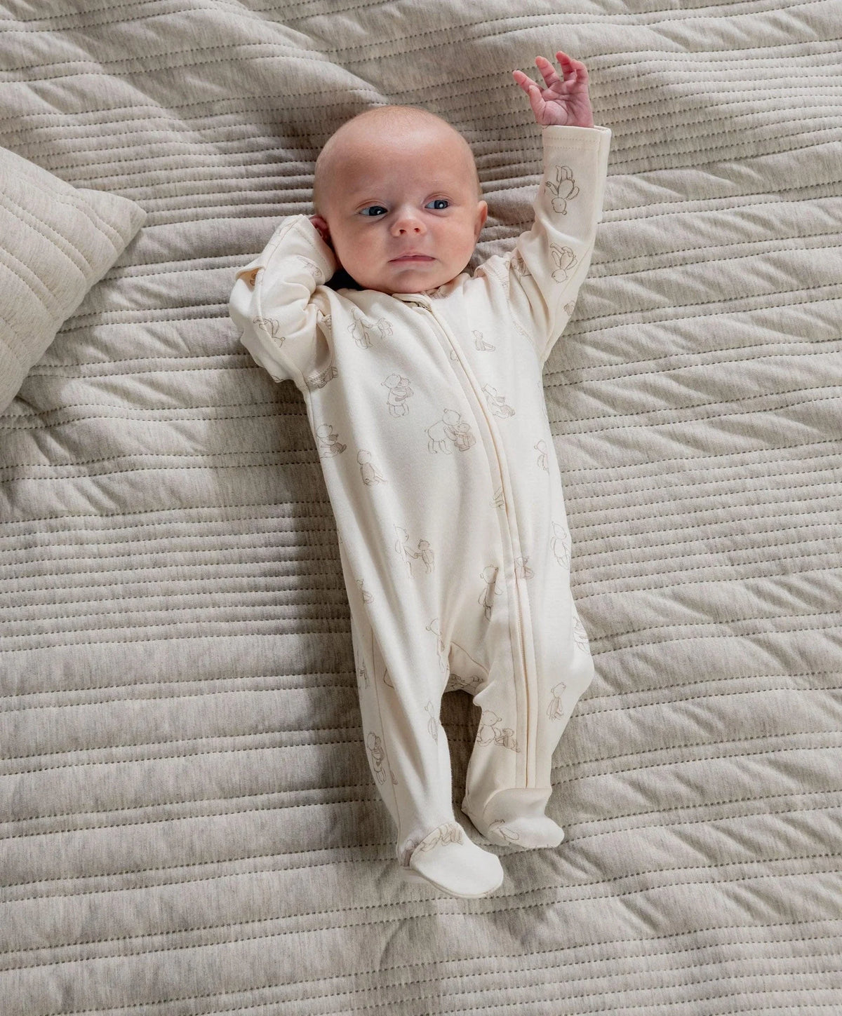 Baby in cream bear-print all-in-one with front zip, long sleeves, open hands