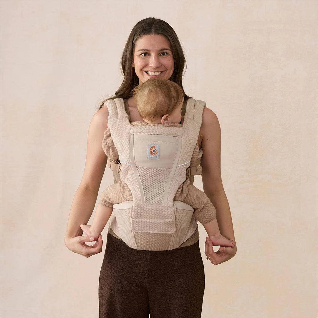 Beige hip seat baby carrier with baby seated in front and padded waist support