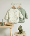 Two long-sleeve baby bibs: cream dinosaur print and sage green bib set.