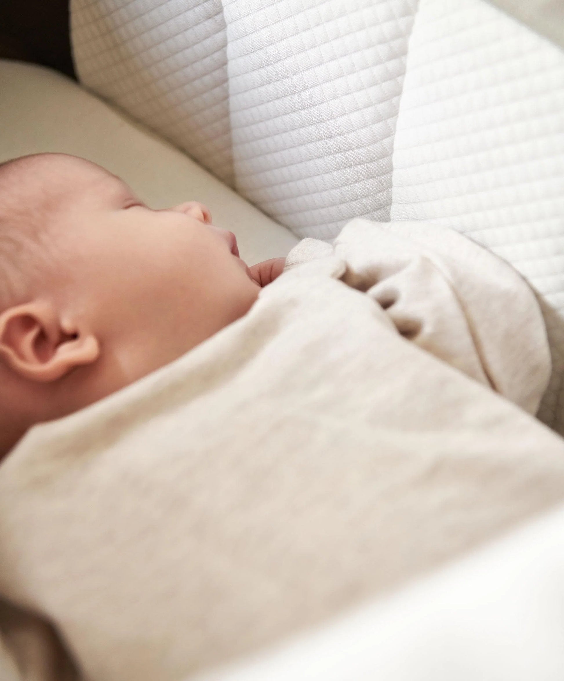 Baby lying in a cream carrycot mattress with quilted bedding